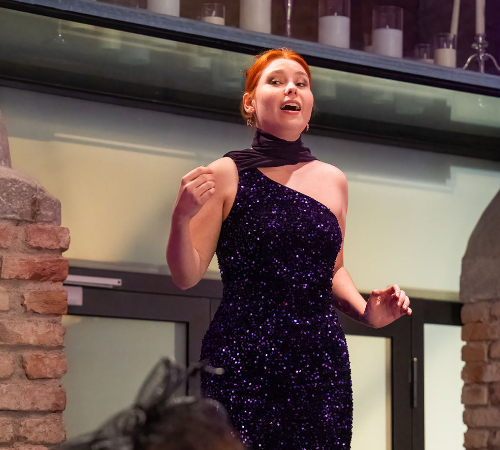 Female student singing in an elegant dress during a performance at The New Academy Musical Theatre Vienna.